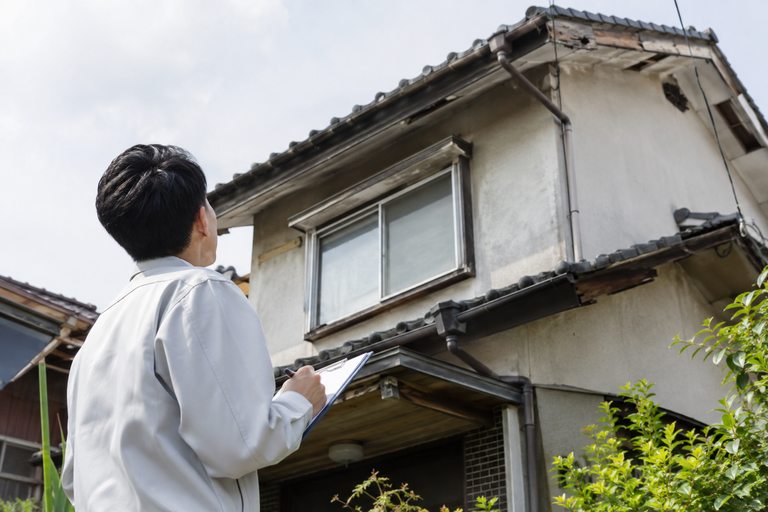 傷んだ住宅の屋根を地上から見上げて確認している人
